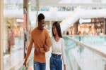 Full body length of romantic millennial African American guy and lady making shopping on weekend walking in the city mall with colorful bags spending time together and talking free copy space iStock 1476002257 banner