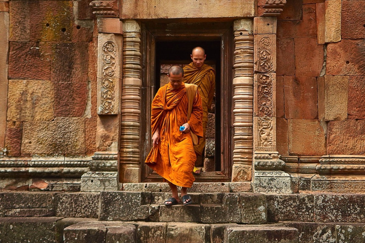 Two monks in orange robes walk out a temple in Thailand